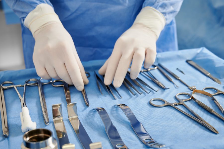 Close up of plastic surgeon in sterile gloves getting ready medical instruments for operation. Doctor preparing scissors, forceps and scalpels for surgery. Concept of plastic surgery preparation.